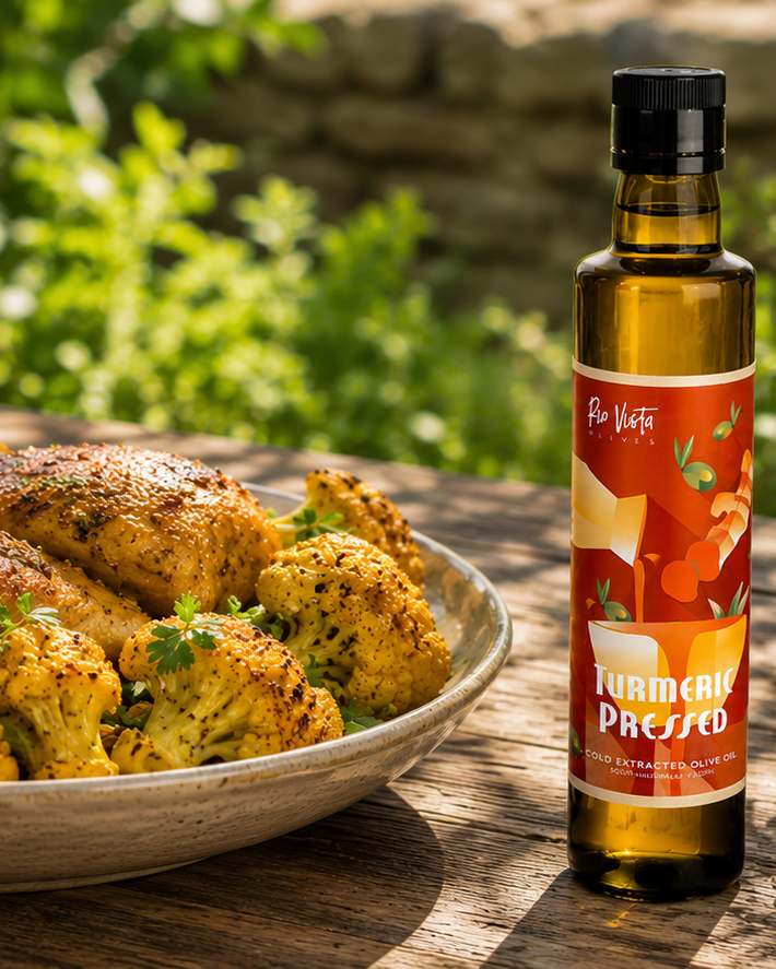Bottle of 'Turmeric Pressed' olive oil next to a bowl of roasted vegetables outdoors.
