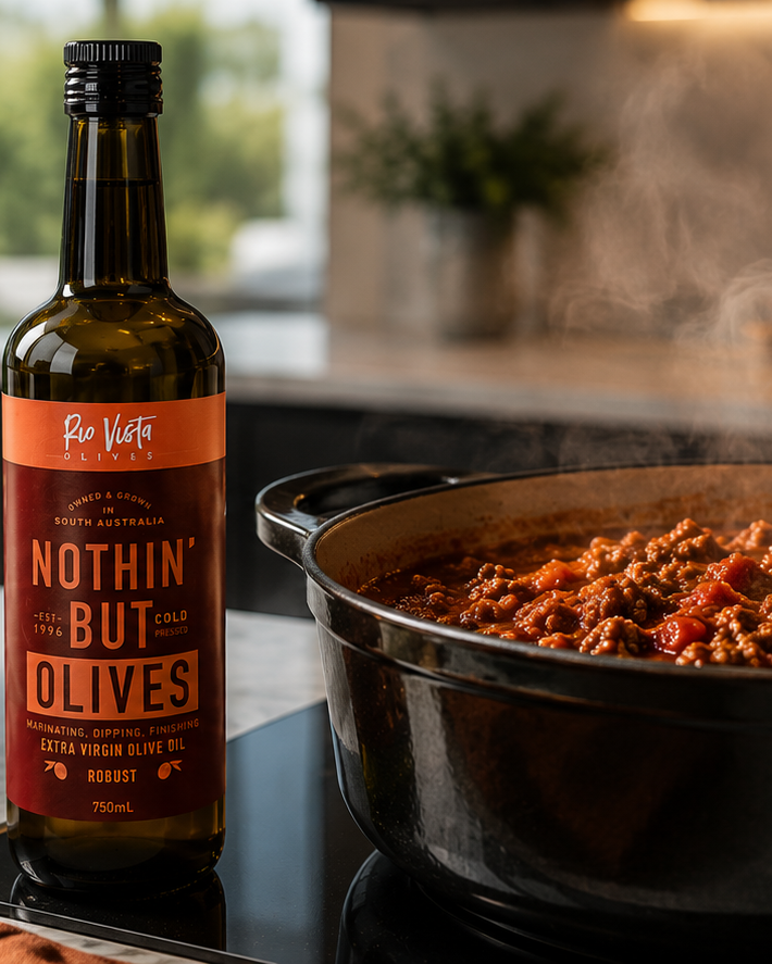 Olive oil bottle on a kitchen counter with a crock pot of chilli and a jar of basil leaves